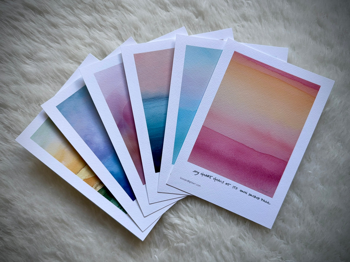 A fan of five art prints from the surgery recovery card set, showcasing gradients of pink, blue, yellow, green, and purple, arranged on a soft white background.